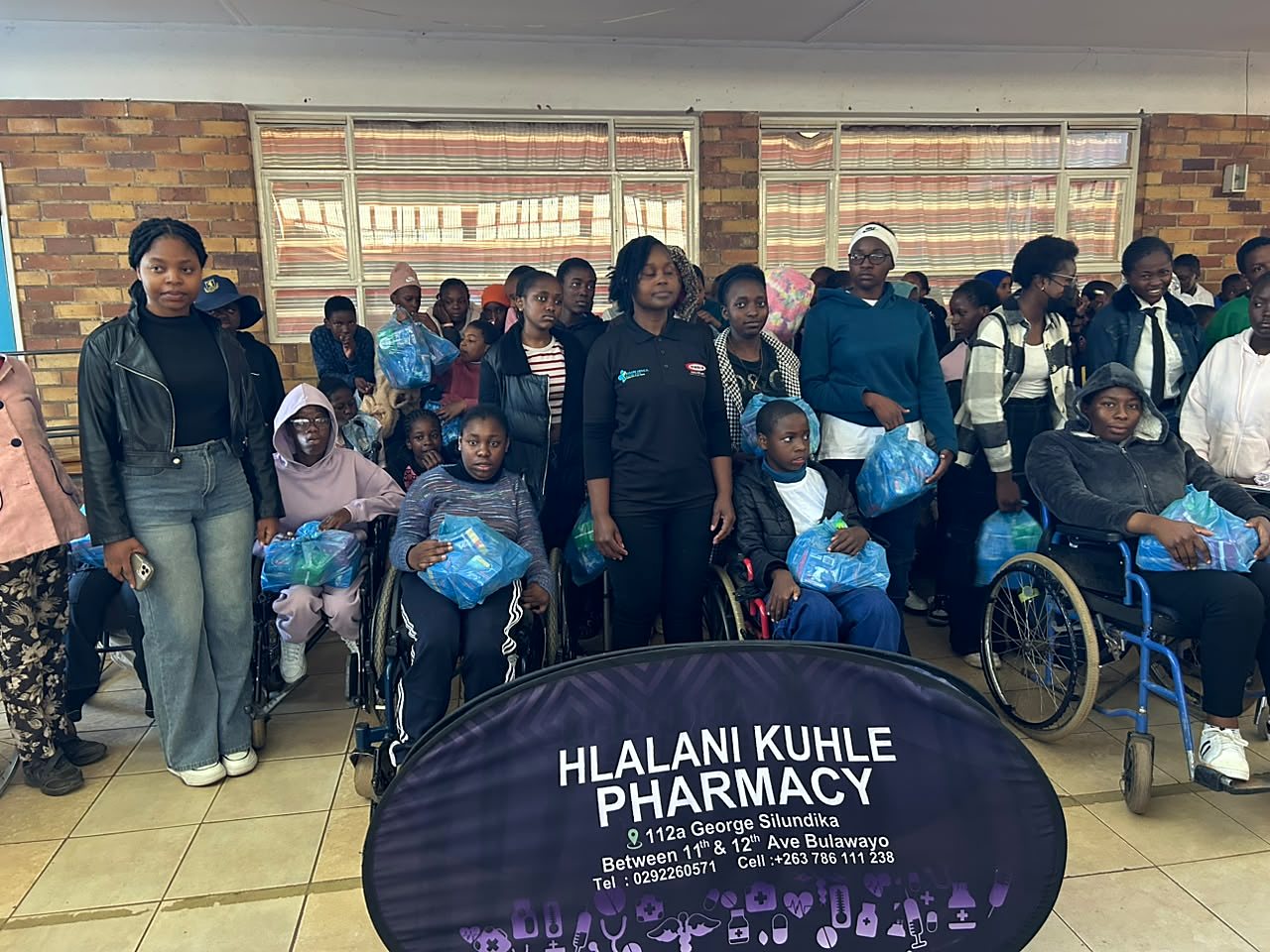Young people and wheelchair users gathered behind a Hlalani Kuhle Pharmacy sign